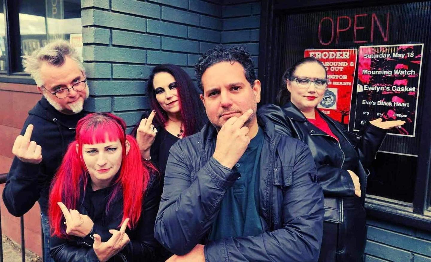 Group band photo of Eve's Black Heart, giving the camera a middle finger outside a music venue